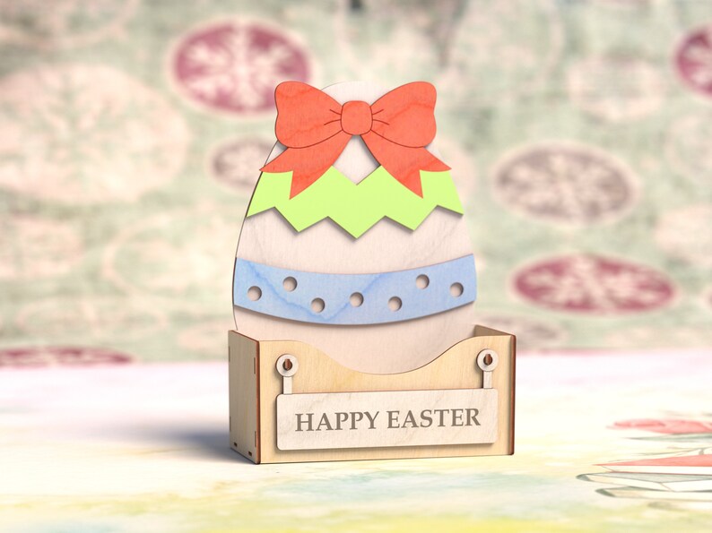 May include: A wooden Easter egg decoration with a green and blue design and a red bow. The egg is sitting on a wooden stand with the words "Happy Easter" written on it.