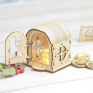May include: A wooden house shaped nightlight with a door that opens and a window with a string of lights inside. The house is sitting on a white surface.