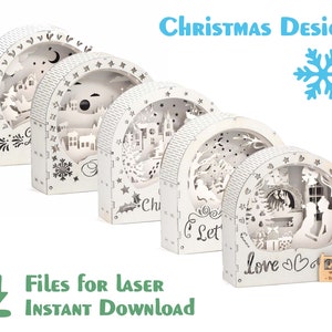 May include: Five white wooden Christmas ornaments with intricate laser cut designs. The ornaments feature winter scenes, including a snowy village, a Christmas tree, and a couple standing in front of a fireplace. The text "Love" is visible on the bottom of one ornament.