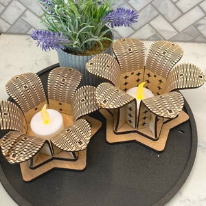 Puede incluir: Dos portavelas de madera con forma de flores con un patr&oacute;n geom&eacute;trico. Cada portavelas tiene una peque&ntilde;a vela de t&eacute; blanca en su interior.