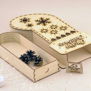 May include: A wooden Christmas stocking box with a drawer and a cutout design of snowflakes. The box has a sign that says "Merry Christmas".