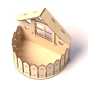 May include: A wooden box shaped like a house with a fence around the bottom and a window in the front. The roof is open and the inside of the box is empty.