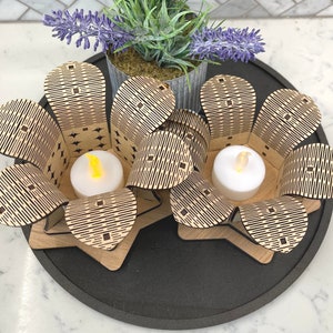 Puede incluir: Dos portavelas de madera con forma de flores con un patr&oacute;n geom&eacute;trico. Cada portavelas tiene una peque&ntilde;a vela de t&eacute; en su interior.