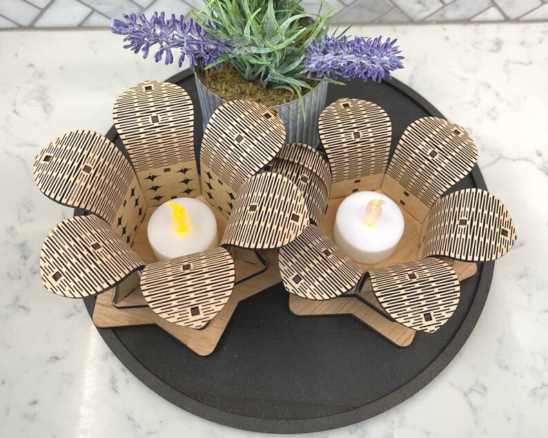 Puede incluir: Dos portavelas de madera con forma de flores con un patr&oacute;n geom&eacute;trico. Cada portavelas tiene una peque&ntilde;a vela de t&eacute; en su interior.