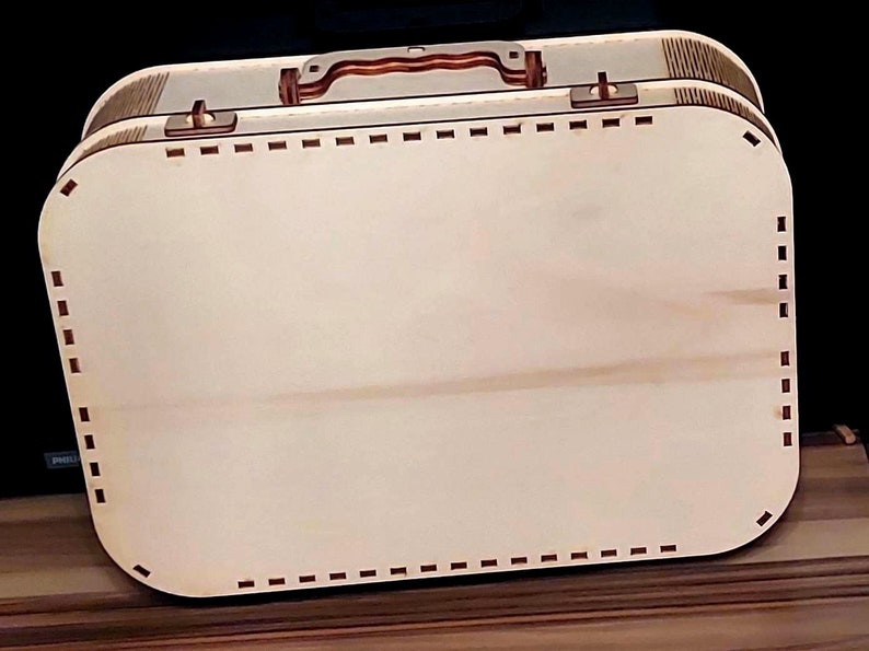 May include: A wooden suitcase with a brown handle and a decorative stitched border. The suitcase is closed and has a light wood finish.