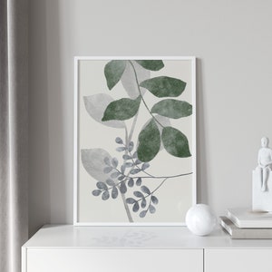 K&ouml;nnte beinhalten: Ein gerahmter Druck eines Aquarells mit einer stilisierten Anordnung von gr&uuml;nen und grauen Bl&auml;ttern auf cremefarbenem Hintergrund.