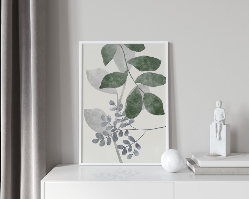 K&ouml;nnte beinhalten: Ein gerahmter Druck eines Aquarells mit einer stilisierten Anordnung von gr&uuml;nen und grauen Bl&auml;ttern auf cremefarbenem Hintergrund.