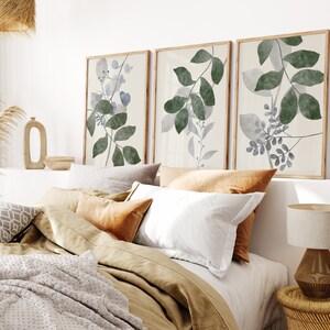 K&ouml;nnte beinhalten: Drei gerahmte Aquarelldrucke von stilisierten gr&uuml;nen und blauen Bl&auml;ttern auf wei&szlig;em Hintergrund. Die Drucke h&auml;ngen &uuml;ber einem Bett mit einer braunen Bettw&auml;sche aus Leinen und wei&szlig;en Kissen.