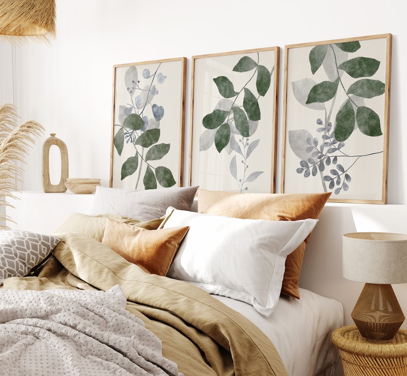 K&ouml;nnte beinhalten: Drei gerahmte Aquarelldrucke von stilisierten gr&uuml;nen und blauen Bl&auml;ttern auf wei&szlig;em Hintergrund. Die Drucke h&auml;ngen &uuml;ber einem Bett mit einer braunen Bettw&auml;sche aus Leinen und wei&szlig;en Kissen.