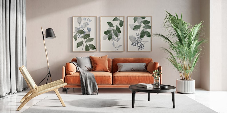 K&ouml;nnte beinhalten: Ein Wohnzimmer-Interieur mit einem braunen Sofa, einem Holzstuhl, einer Stehlampe, einem Couchtisch, einer Topfpflanze und drei gerahmten botanischen Drucken an der Wand.