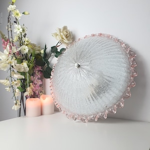 May include: A round, clear glass ceiling light fixture with a textured, ribbed surface and a ruffled, light pink glass edge. The fixture features a central white knob and a domed shape, designed to be mounted flush against a ceiling surface.