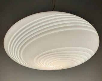 Puede incluir: Una lámpara colgante circular grande de color blanco con una superficie de vidrio esmerilado liso. La pantalla presenta un patrón en espiral elevado y distintivo que irradia desde el centro hacia los bordes, creando un efecto texturizado.