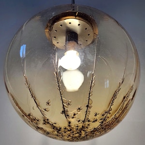 May include: A vintage, spherical pendant light fixture. The clear glass globe features a warm amber hue and is adorned with a delicate, botanical design in a darker shade. The fixture includes a brass-toned metal cap and a visible light bulb.