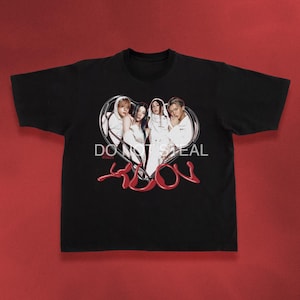 May include: Black t-shirt featuring a graphic of four people in white outfits inside a heart-shaped frame. The text "DO NOT STEAL" is above the heart, with the word "SOON" in red script below.