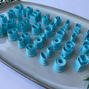 Puede incluir: Un juego de 30 cortadores de galletas de pl&aacute;stico azul en varias formas, incluyendo c&iacute;rculos, cuadrados, rect&aacute;ngulos, tri&aacute;ngulos y m&aacute;s. Los cortadores est&aacute;n dispuestos en un plato gris.