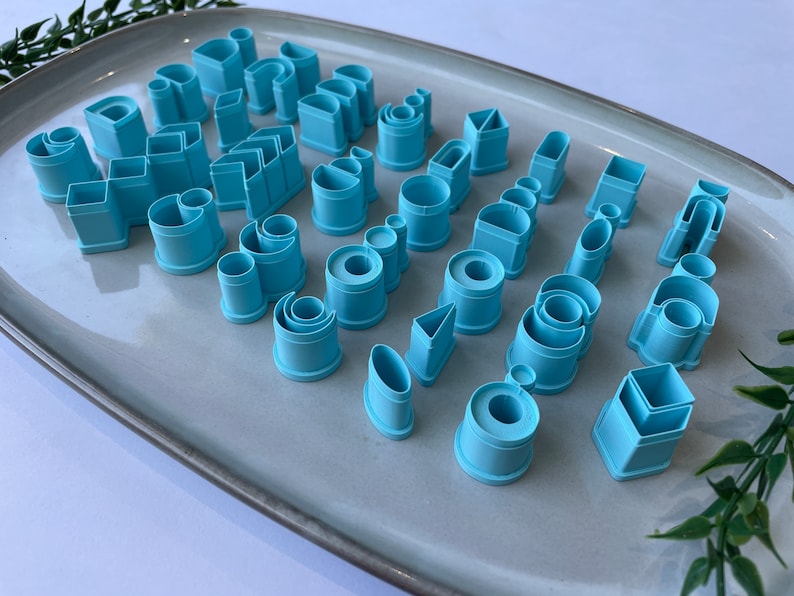 Puede incluir: Un juego de 30 cortadores de galletas de pl&aacute;stico azul en varias formas, incluyendo c&iacute;rculos, cuadrados, rect&aacute;ngulos, tri&aacute;ngulos y m&aacute;s. Los cortadores est&aacute;n dispuestos en un plato gris.