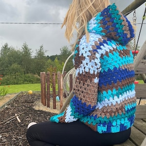 May include: A hooded crocheted sweater with a colourful striped pattern in shades of blue, brown, and turquoise.