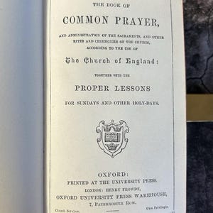 May include: Open book titled "The Book of Common Prayer" with text in black ink. The book's title is centered at the top, with additional text below. The book is open to a page with a decorative emblem and the publisher's information.