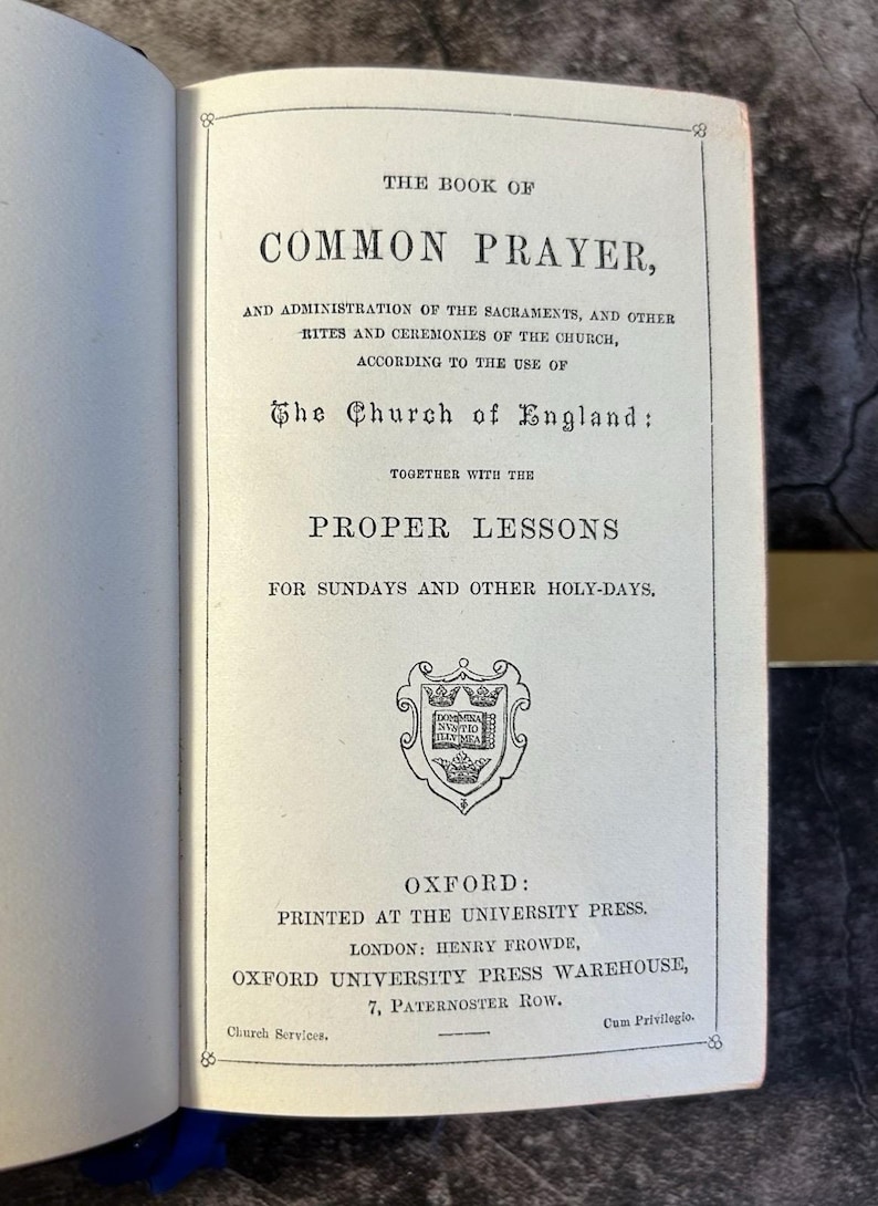 May include: Open book titled "The Book of Common Prayer" with text in black ink. The book's title is centered at the top, with additional text below. The book is open to a page with a decorative emblem and the publisher's information.