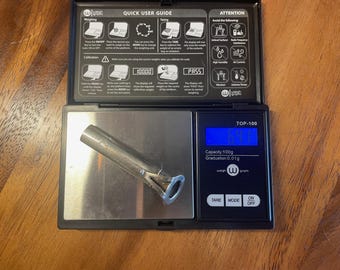 May include: A silver metal nozzle on a black digital scale displaying "TOP-100", "Capacity: 100g", "Graduation 0.01g", "TARE", "MODE", "ON", and "OFF".