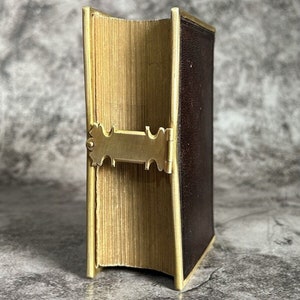 May include: A closed book with a brown leather cover and gold trim. The book has a decorative brass clasp.