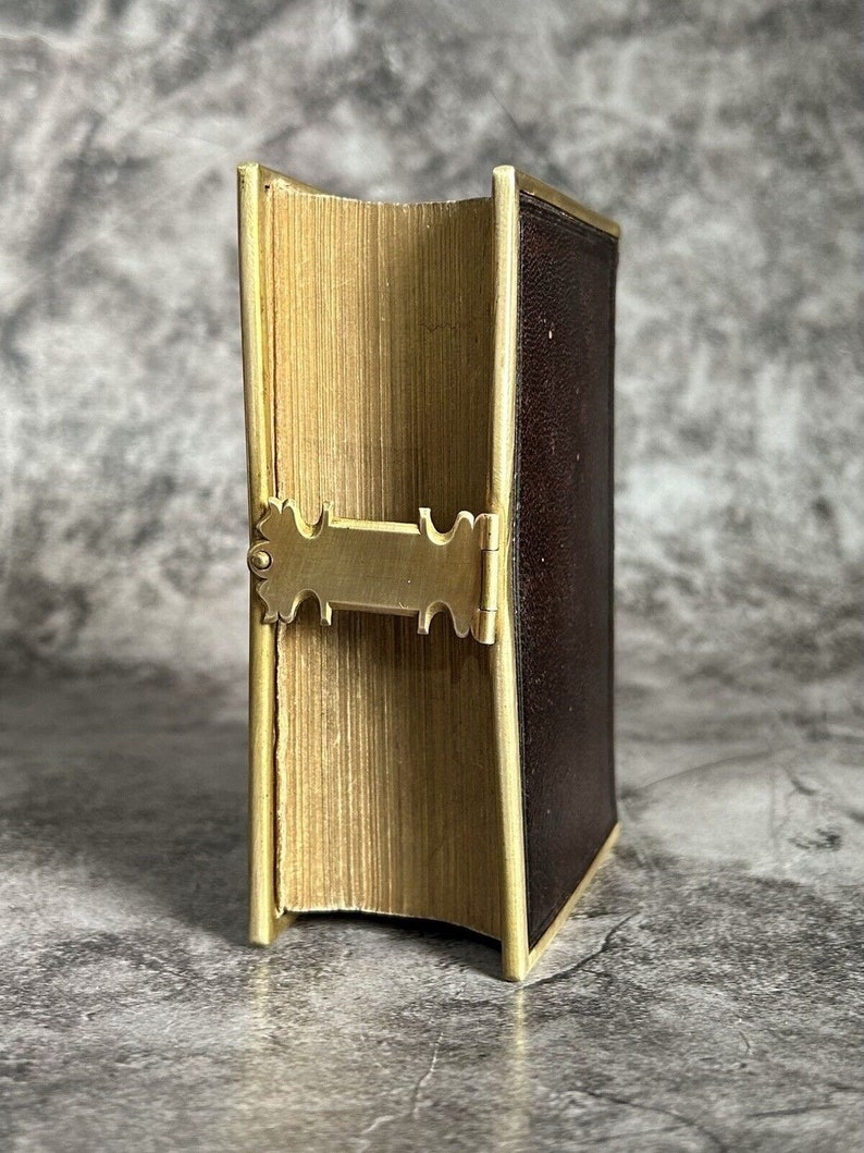 May include: A closed book with a brown leather cover and gold trim. The book has a decorative brass clasp.