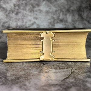 May include: A gold-colored book with a decorative clasp. The book is closed and has a textured cover.