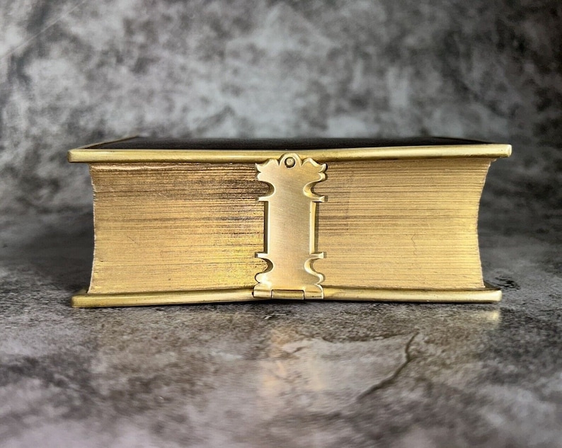 May include: A gold-colored book with a decorative clasp. The book is closed and has a textured cover.