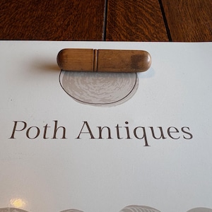 May include: A light-colored wooden object with a rounded shape, resting on a white surface. The text "Poth Antiques" is printed in brown. The object appears to be a handle or a small tool.