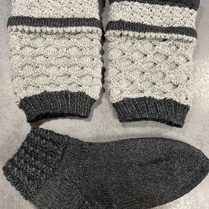 May include: A pair of grey and black knitted leg warmers with a diamond pattern and a black knitted sock.