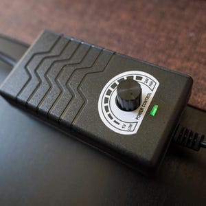 Pu&ograve; includere: Unit&agrave; di controllo dell'alimentazione nera con una manopola rotonda e una luce verde. La manopola &egrave; contrassegnata con "Low", "12V", "24V" e "High".