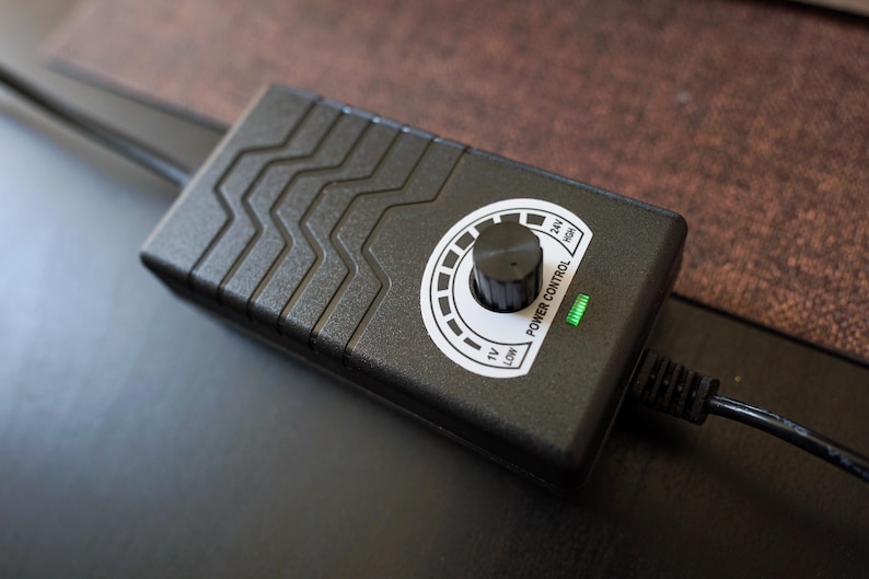 Pu&ograve; includere: Unit&agrave; di controllo dell'alimentazione nera con una manopola rotonda e una luce verde. La manopola &egrave; contrassegnata con "Low", "12V", "24V" e "High".