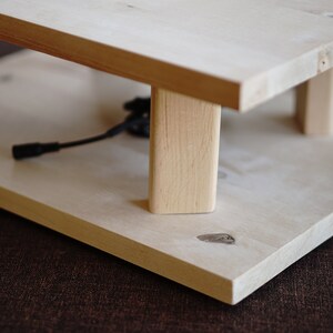 Pu&ograve; includere: Un supporto in legno con due ripiani, realizzato in legno chiaro. Il supporto ha un design semplice con quattro gambe e una forma rettangolare.