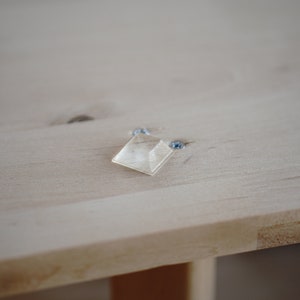 Pu&ograve; includere: Un quadrato di plastica trasparente con bordi arrotondati &egrave; fissato a una superficie in legno chiaro con due viti.