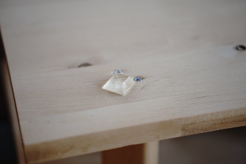 Pu&ograve; includere: Un quadrato di plastica trasparente con bordi arrotondati &egrave; fissato a una superficie in legno chiaro con due viti.