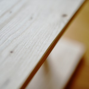 Pu&ograve; includere: Primo piano di uno scaffale in legno chiaro con una superficie liscia e leggermente strutturata. Lo scaffale &egrave; inclinato e sembra far parte di un mobile pi&ugrave; grande.