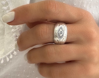 Può includere: Anello d'argento con una fascia testurizzata e un design di occhio malvagio. L'anello è indossato su un dito.