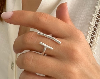 May include: A silver ring with two textured bars, one horizontal and one angled, forming a unique design.