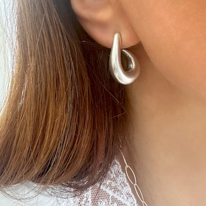 以下が含まれることがあります： ユニークな涙の形をしたシルバーのフープピアス。ピアスは滑らかで、磨かれた仕上げになっています。