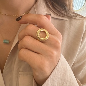 Peut inclure: Une bague en or avec un grand motif rond ouvert. La bague est portée à l'index.