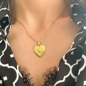 Könnte beinhalten: Eine goldene Halskette mit einem herzförmigen Anhänger, der auf der Vorderseite ein kleineres Herzdesign aufweist.