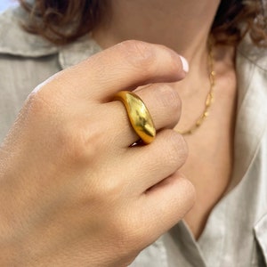 Peut inclure: Une bague en or avec une forme ovale lisse et arrondie. La bague est épaisse et a une finition brossée.