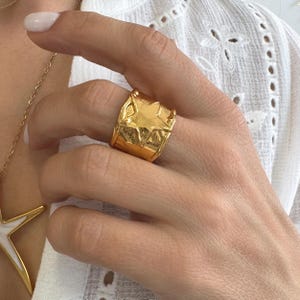 Può includere: Un anello dorato e massiccio con un design a stella. L'anello presenta una superficie strutturata e un aspetto audace. La stella è ben visibile sulla parte anteriore, aggiungendo un tocco di fascino celeste a questo gioiello.