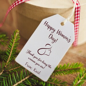 May include: A white gift tag with the text "Happy Women's Day!" and "Thank you for being the woman you are!"  The tag also includes a stylized image of a woman's face and the text "From: Karl".