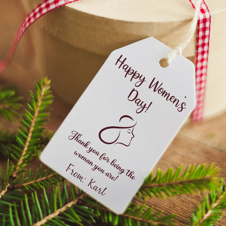 May include: A white gift tag with the text "Happy Women's Day!" and "Thank you for being the woman you are!"  The tag also includes a stylized image of a woman's face and the text "From: Karl".