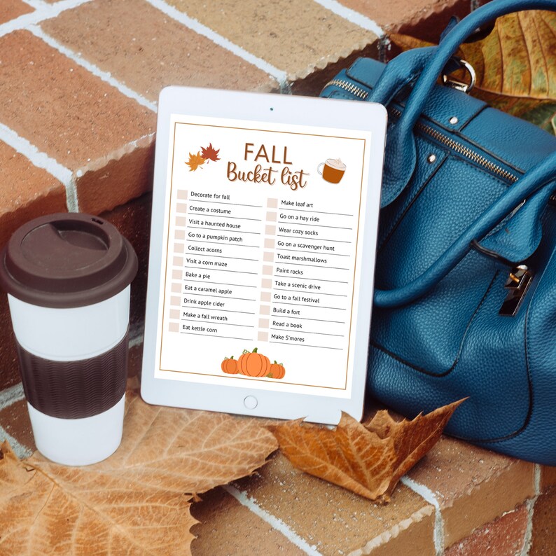 Puede incluir: Una tableta digital que muestra una lista de cosas que hacer en oto&ntilde;o con actividades como decorar para el oto&ntilde;o, crear un disfraz, visitar una casa encantada, ir a un huerto de calabazas, recoger bellotas, visitar un laberinto de ma&iacute;z, hornear un pastel, comer una manzana caramelizada, beber sidra de manzana, hacer una corona de oto&ntilde;o y comer palomitas de ma&iacute;z. La tableta est&aacute; sobre una superficie de ladrillo con una bolsa azul y hojas de oto&ntilde;o.