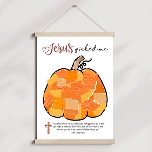 K&ouml;nnte beinhalten: Gerahmter Druck mit einem gro&szlig;en orangefarbenen K&uuml;rbis aus Papierst&uuml;cken. Der Text "Jesus picked me" steht oben, mit einem Bibelvers und einem Kreuz unten. Der Druck h&auml;ngt an einer Holzstange.
