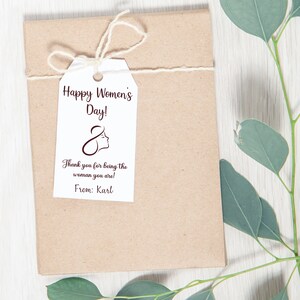 May include: A white gift tag with brown text that reads "Happy Women's Day!" and "Thank you for being the woman you are!" with a stylized female figure and the text "From: Karl".