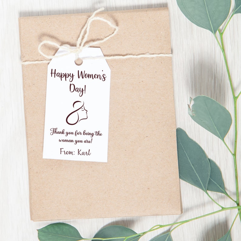 May include: A white gift tag with brown text that reads "Happy Women's Day!" and "Thank you for being the woman you are!" with a stylized female figure and the text "From: Karl".