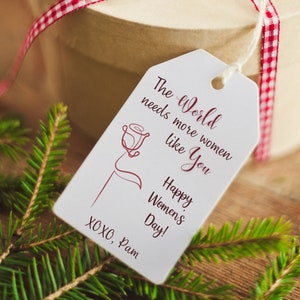 May include: White gift tag with a red rose illustration and the text "The World needs more women like You Happy Women's Day! XOXO, Pam"